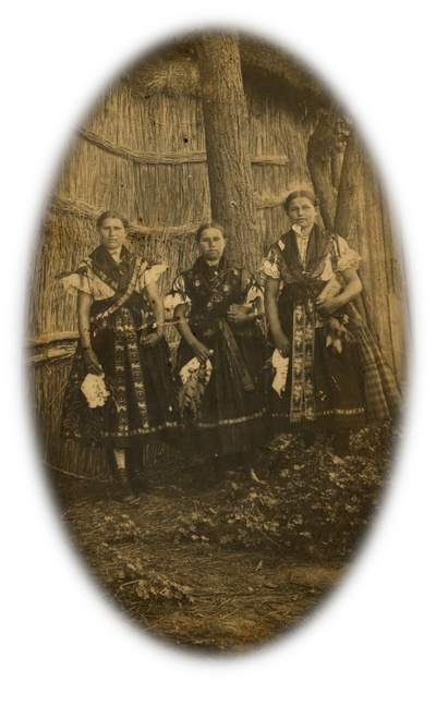  Kostoľany girls in traditional costumes from the beginning of the 20th century in front of a farm building with post-in-the-ground construction and wattle-and-daub panels