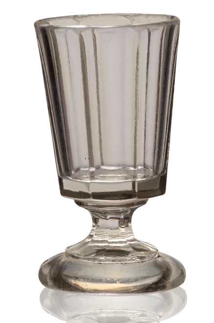 Hrubostenný kalíšok na tvrdý alkohol, s hranovanou, kónickou kupou, na nízkej nohe a kruhovom podstavci. Fúkané číre sklo zo 60. rokov 19. storočia